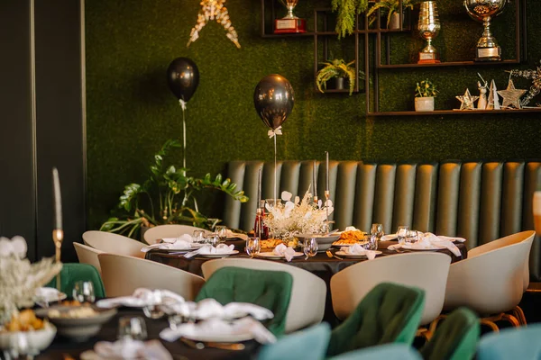 stock image Riga, Latvia - December 6, 2023 - an elegantly set table with white floral arrangements, black balloons with bow ties, and a greenery wall with trophy shelves in the background.