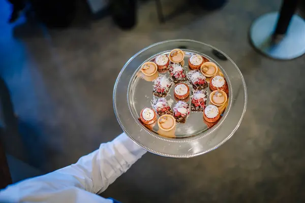 server\'s hand holding a tray of assorted canaps, with a focus on the elegant presentation and variety of the small bites.