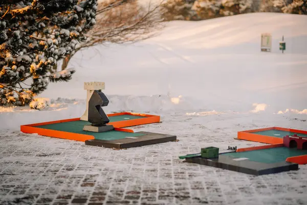 Riga, Latvia - December 6, 2023 -  snow-covered mini-golf course with colorful obstacles and a large chess piece-like structure, with a wintry background.