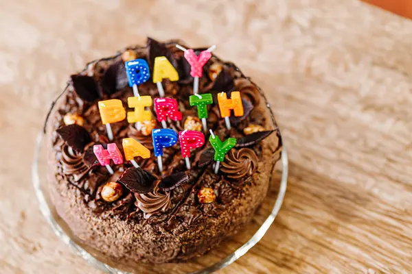 chocolate cake with HAPPY BIRTHDAY spelled out in colorful letter candles on a wooden table.