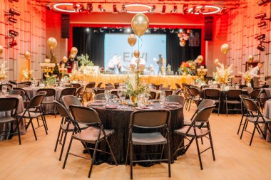 Bir gala, ışıltılı masa örtüleri, altın balonlar ve arka planda sanatçıların olduğu bir sahne için hazırlanan şenlik salonu..