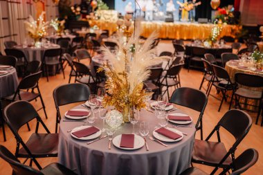  bir etkinlik için altın süslemeler ve sofra takımı ile dekore edilmiş bir masa, arka planda bir grup sahne alıyor..