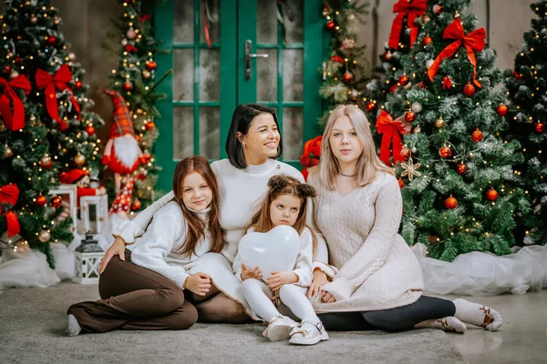 mother and three daughters seated in front of a festive Christmas tree, smiling and looking towards the camera.