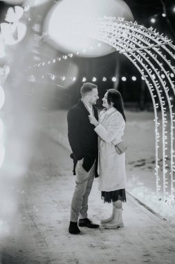 Geceleri karla kaplı bir ortamda ışıkların bokeh etkisi ile çevrili bir çift birbirlerine yakın duruyorlar..