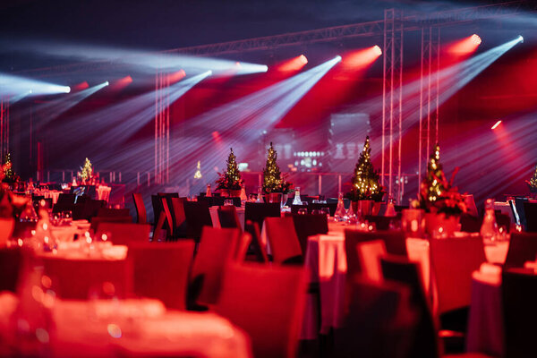 elegant event space with tables adorned with Christmas trees and festive lighting casting dynamic shadows.