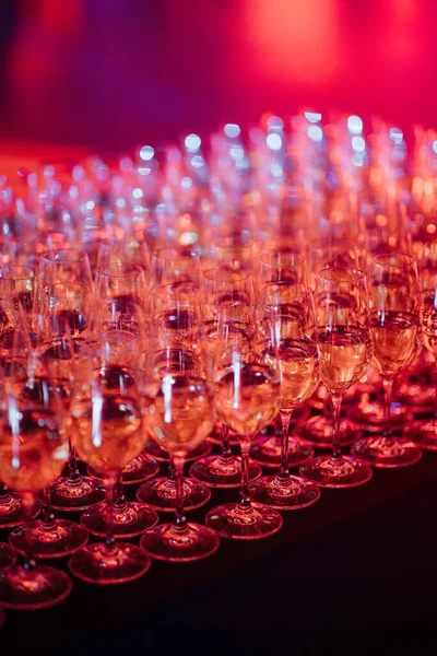 multitude of wine glasses filled with a light pink liquid, set against a vibrant red backdrop.