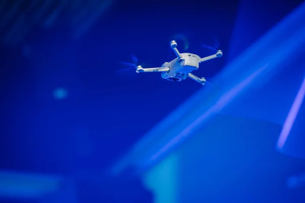 drone in flight against a blue-lit background, with light rays visible around it.
