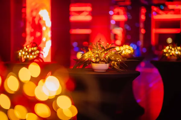 close-up of a festive table centerpiece with lights and blurred bokeh background in a red-toned event space.