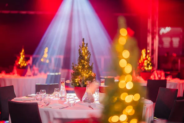 festive event setting with tables, lit Christmas trees, and a bokeh effect from the lights, under a wash of red and blue lighting.