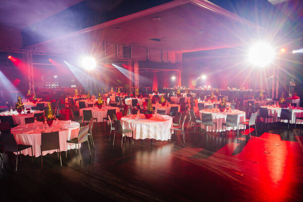 large event hall with set dining tables, festive centerpieces, and bright stage lighting illuminating the space.