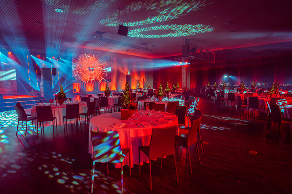 banquet hall with festive tables, a lit Christmas tree centerpiece, and a striking light display with blue and red lights.