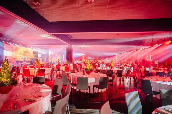 festively decorated banquet hall with tables, Christmas trees, and vibrant red and blue lighting