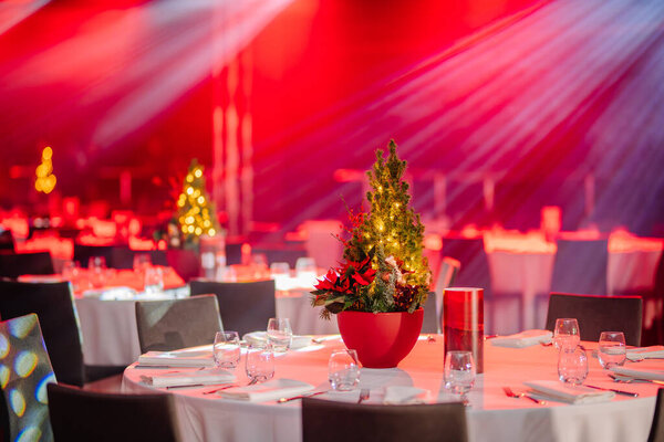 decorated table with a Christmas tree centerpiece, set for a festive event, under red stage lighting.