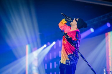 Riga, Letonya - 18 Aralık 2023 - Sahnede bir mikrofona şarkı söyleyen dinamik sahne aydınlatması onu arkadan vurguluyor..