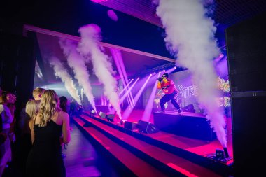 Riga, Letonya - 18 Aralık 2023 - Seyirci izlerken yoğun duman ve ışık efektleriyle sahnede performans sergileyen sanatçı.