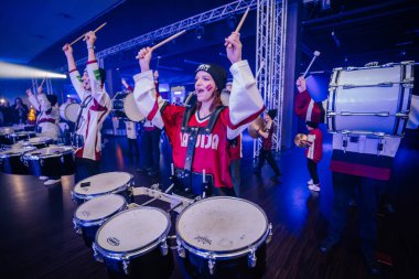 Riga, Letonya - 18 Aralık 2023 - canlı Letonyalı hokey fanatik bateristleri mavi ışıklı bir mekanda coşkuyla şarkı söylüyorlar..