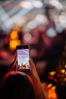 Riga, Letonya - 18 Aralık 2023 - arka planda bulanık ışıklar ve fotoğraf çeken akıllı telefonlu ellerin yakın çekimi.