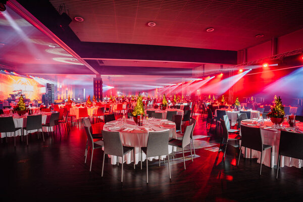 Riga, Latvia - December 18, 2023 - banquet hall with tables set for an event, highlighted by dramatic red and blue stage lighting.