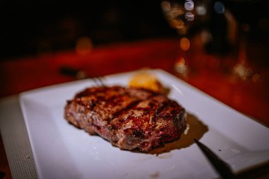 Malaga, İspanya - 21 Ocak 2024 - Yanı beyaz bir tabakta ızgara bifteğin yakın çekimi, arka planda bokeh olan bir restoranda.