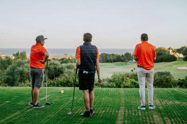 Malaga, İspanya - 21 Ocak 2024 - 3 golfçü bir golf sahasında denize bakan, ağaçlar ve açık gökyüzüyle.