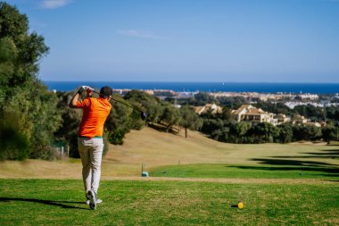 Malaga, İspanya - 21 Ocak 2024 Açık gökyüzü olan kıyı manzarasına bakan golf sahasında sallanan bir golfçü.