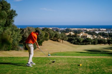 Malaga, İspanya - 21 Ocak 2024 Açık gökyüzü olan kıyı manzarasına bakan golf sahasında sallanan bir golfçü.