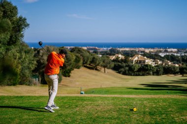 Malaga, İspanya - 21 Ocak 2024 Açık gökyüzü olan kıyı manzarasına bakan golf sahasında sallanan bir golfçü.