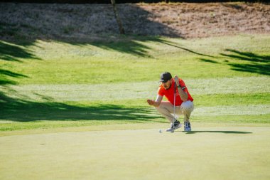 Malaga, İspanya - 21 Ocak 2024 - Kırmızı ve beyaz giyinmiş odaklanmış bir golfçü golf sahasına çömelmiş durumda..