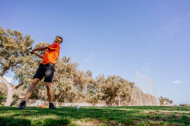 Malaga, İspanya - 21 Ocak 2024 Turuncu gömlekli bir golfçü golf sahasındaki açık gökyüzü ve ağaçlardan oluşan bir zemine doğru sallanırken yakalandı.