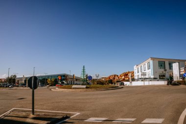 Malaga, İspanya - 21 Ocak 2024 - Mavi gökyüzü altındaki yol işaretleri, süpermarket ve konut binalarıyla dolu sakin bir kavşakta açık bir gün.