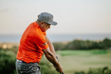 Malaga, İspanya - 21 Ocak 2024 - Golf salıncağının ortasında, turuncu gömlekli, gri pantolonlu ve gri şapkalı bir adamın yakın plan fotoğrafı.