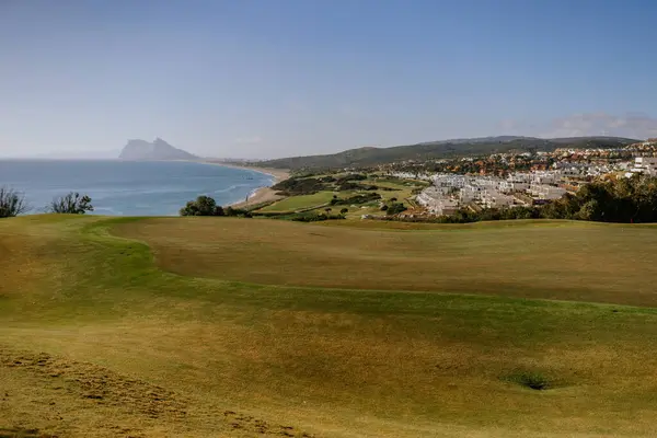 Sotogrande, Spain - January, 23, 2024 - A scenic coastal golf course with a prominent rock formation in the distance, overlooking a beach and residential area.