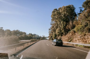 Santa Margarita, İspanya - 24 Ocak 2024 - Ağaçlarla kaplı bir otoyol ve manzaralı başka bir araba gösteren bir araçtan gündüz vakti yol sahnesi