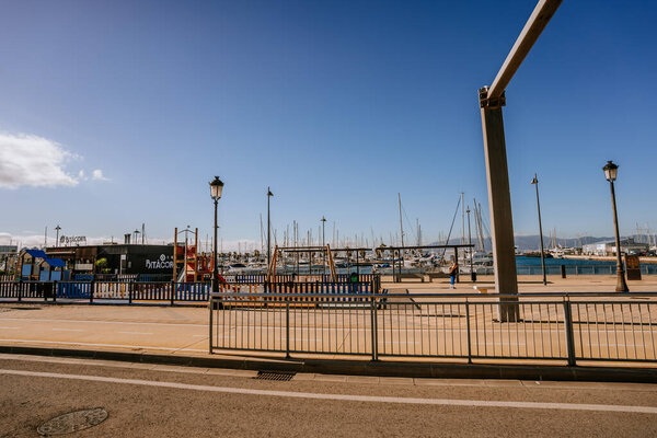 Санта-Фелита, Испания - 24 января 2024 года - набережная с пальмовыми деревьями, пристанищем для лодок, ясным небом и детской игровой площадкой на виду.