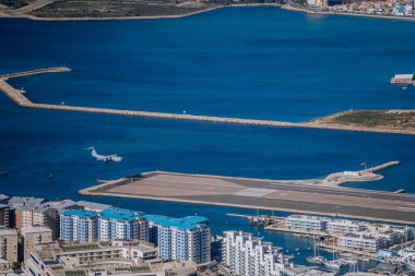 Cebelitarık, İngiltere - 24 Ocak 2024 - bitişik marina, konut binaları ve berrak mavi suları olan bir deniz kenarı havaalanı manzarası. düz iniş