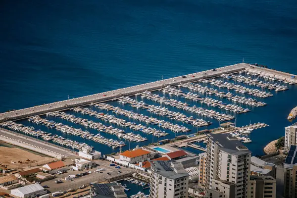 Gibraltar, Britain - January 24, 2024 - Aerial view of a marina with rows of boats and surrounding buildings by the blue sea.