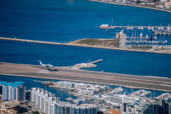 Gibraltar, Britain - January 24, 2024 - A plane landing on a narrow runway by the sea, near a marina full of boats, with apartment buildings nearby.