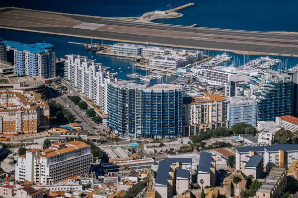 Gibraltar, Britain - January 24, 2024 - Aerial shot of a marina with yachts, surrounded by modern buildings, near an airstrip, against a backdrop of the sea.