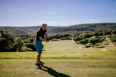 Sotogrante, İspanya - 25 Ocak 2024 - Ağaçlı ve tepeli yemyeşil bir golf sahasına bakan golf sahasında sallanan bir golfçü