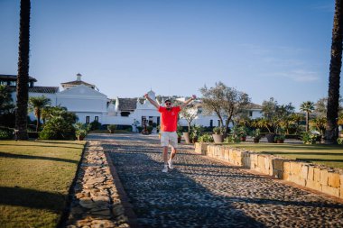 Sotogrante, İspanya - 27 Ocak 2024 - kaldırım taşı yolda yürüyen kolları olan adam, fayanslı çatıları ve arka planda palmiye ağaçları olan beyaz binalar.