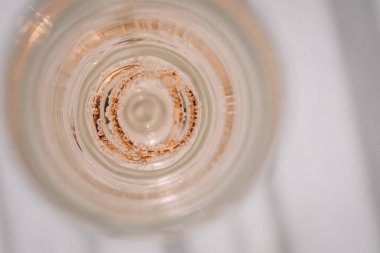 Valmiera, Letonya - 7 Temmuz 2023 - Işıl ışıl bir sıvıyla dolu bir bardaktaki iki alyansın yukarıdan görünüşü.