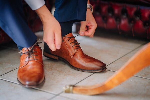 Valmiera, Latvia - July 7, 2023 - A person is tying the laces of brown leather shoes on a tiled floor.
