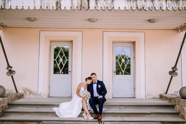 Valmiera, Latvia - July 7, 2023 - Bride and groom seated on steps between two doors, bride resting head on grooms shoulder