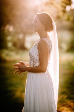 Valmiera, Letonya - 7 Temmuz 2023 - Profilde bir gelin, güneşle yıkanmış, peçeyle gülümsüyor, bir parkta.