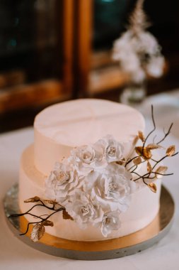 Valmiera, Letonya - 7 Temmuz 2023 - Beyaz çiçekler ve altın yapraklarla süslenmiş iki katlı düğün pastası.