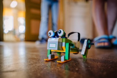 Valmiera, Letonya - 28 Haziran 2023 - Parlak zeminde geniş gözlü ve tekerlekli oyuncak bir robot, arka planda insanların olduğu bir koridorda.
