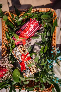 Jurmala, Letonya - 25 Temmuz 2023 - Yeşil yapraklar, kırmızı kurdeleli el yapımı tekstil ve çiçekler içeren bir hasır sepet.