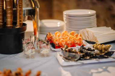 Riga, Letonya - 18 Ocak 2024 - Karides kokteylli yemek masası, kadehli salatalar, zeytinler ve beyaz tabaklar.