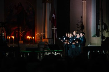Valmiera, Letonya - 7 Ocak 2024 - Saint Simon Kilisesi. Kilise korosu şarkı söylüyor. Arka planda mum ve sunak resmi var. Seyirciler bunu izliyor..