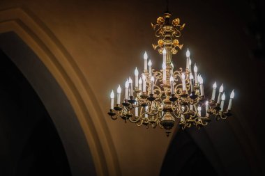 Valmiera, Letonya - 7 Ocak 2024 - Saint Simon Kilisesi. Ilık ışık ve gölgelerle dolu kemerli bir iç kısımda yanan mumlarla süslü bir avize..